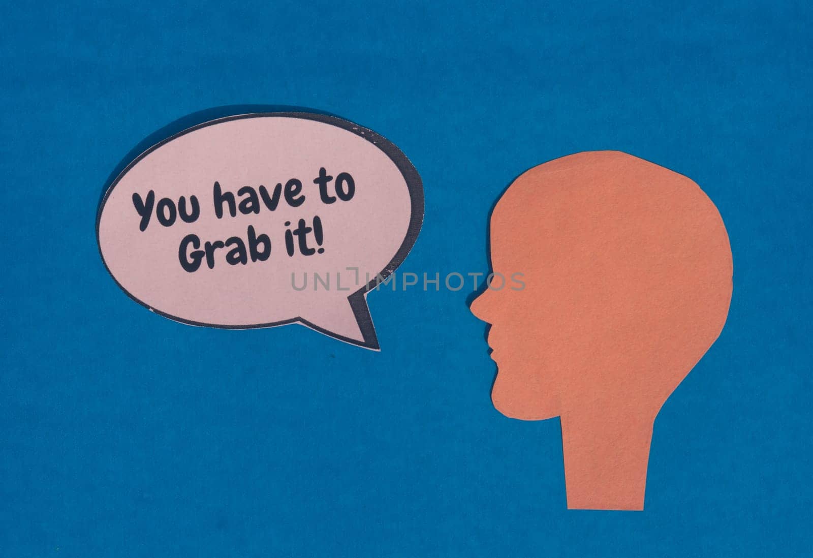 Paper human face with motivation text on speech bubble isolated on blue background. Conceptual image shows strength protest power and revolution.