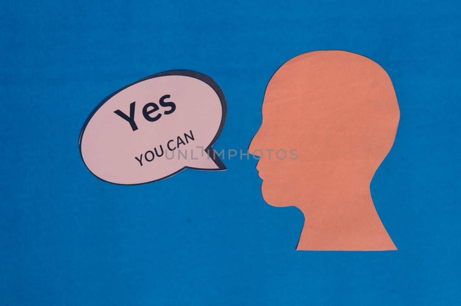 Paper human face with motivation text Yes You Can on speech bubble isolated on blue background. Conceptual image speaker acknowledges that you have the capacity, strength and determination to do.