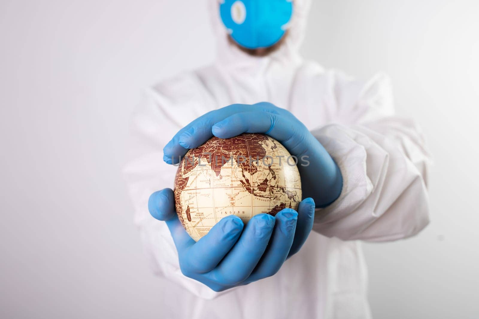World epidemic danger concept. Male doctor man in medical face mask and gloves protecting planet Earth.