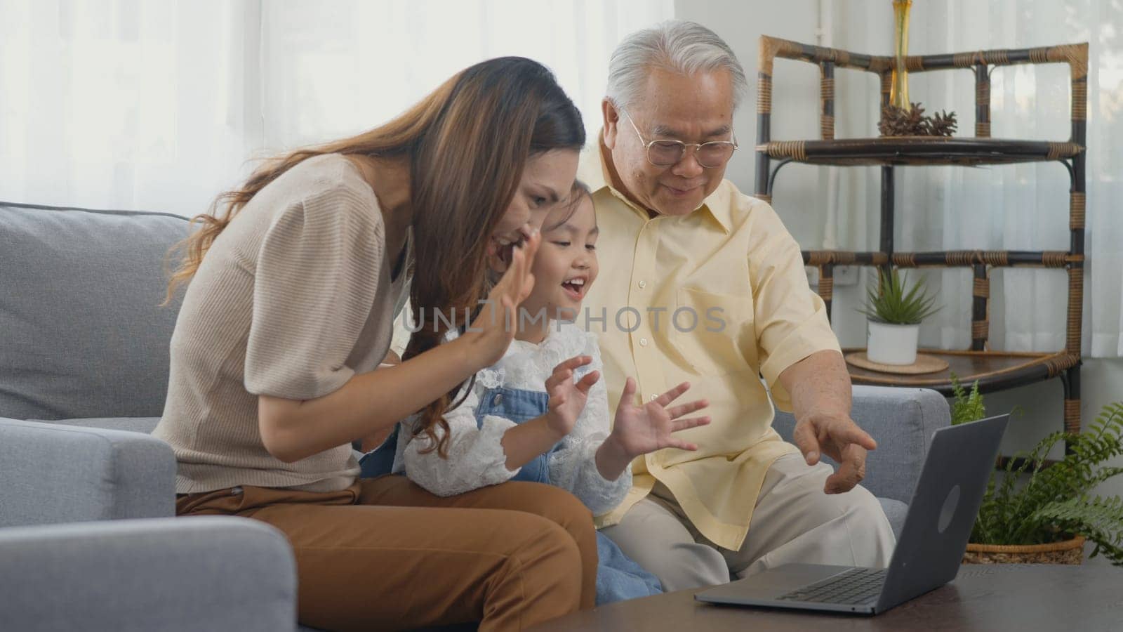Happy family senior grandfather, daughter and granddaughter talking online via video chat using laptop computer with father, old grandpa embracing little grand child and mother in living room at home