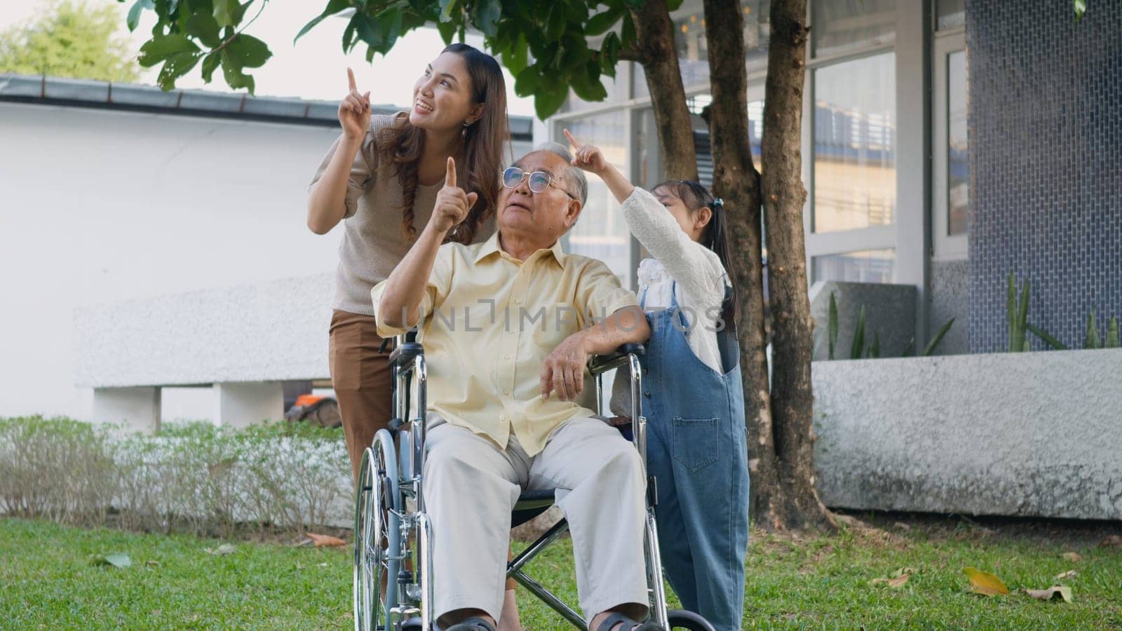 Disabled senior grandpa on wheelchair with grandchild and mother in park, Happy Asian three generation family having fun together outdoors backyard, Grandpa and little child smiling and laughed