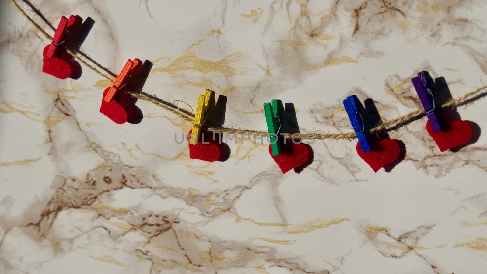 Happy Valentines Day LGBTQIA, colored rainbow clothespins with red hearts and text, on marble background close up.