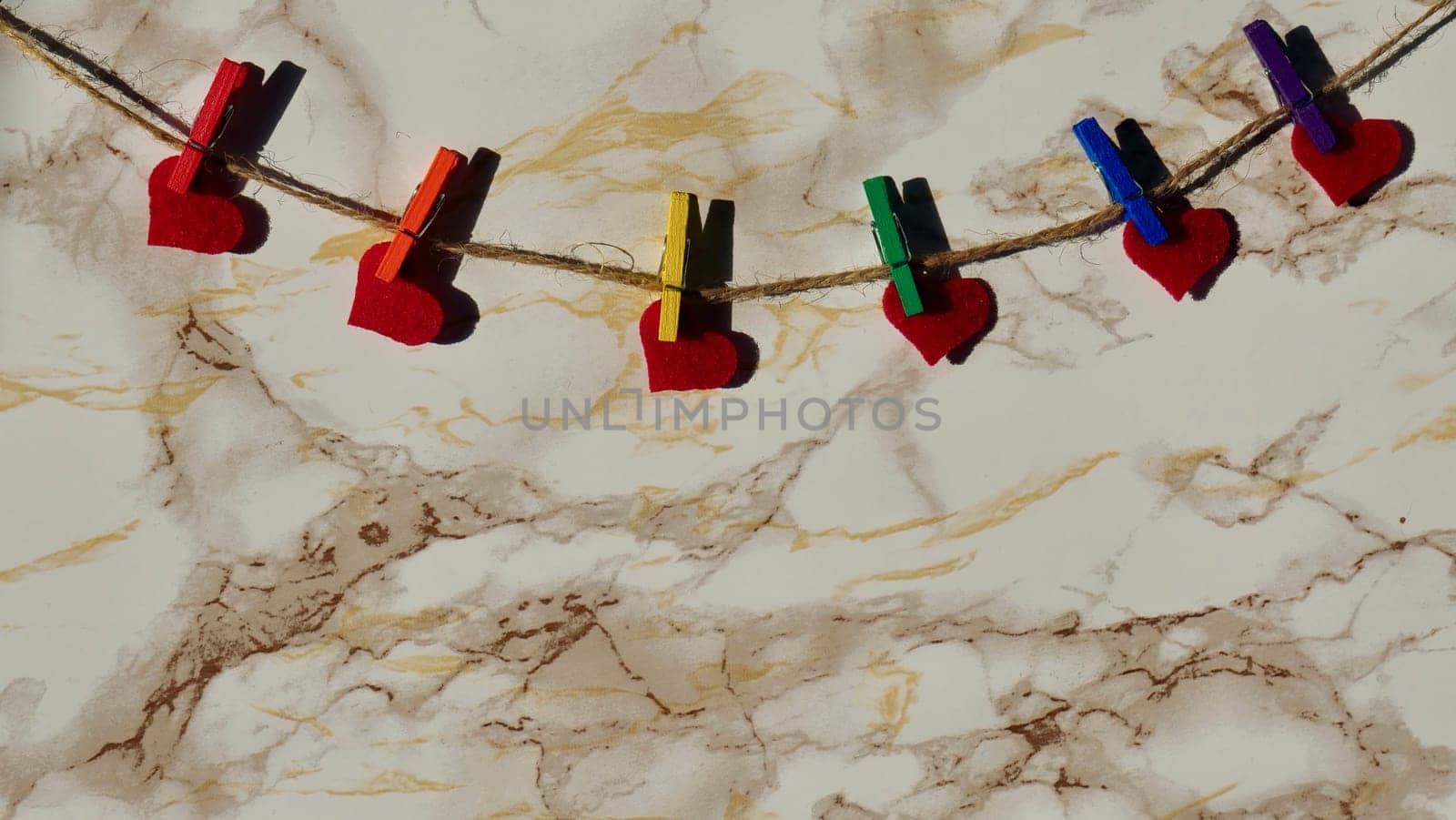 Happy Valentines Day LGBTQIA, colored rainbow clothespins with red hearts and text, on marble background close up.
