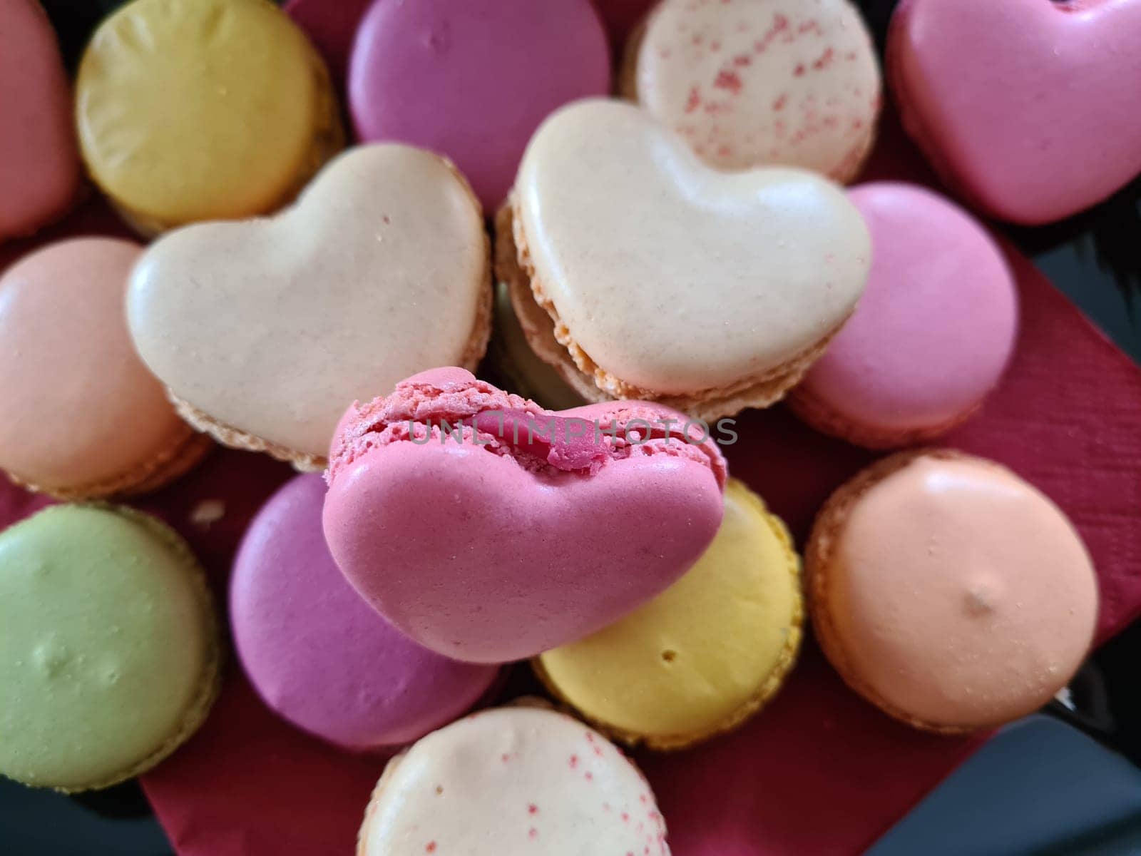 Top view of three delicious macarons and love heart symbol on napkin on wooden table. Romantic vintage valentines day and wedding background