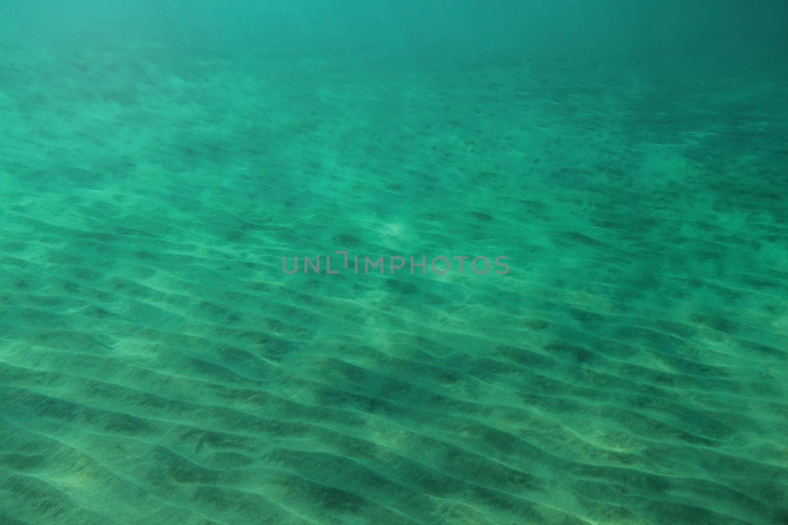 Sea bottom, small "dunes"" in sand lit by sun shining from above. Abstract marine background."