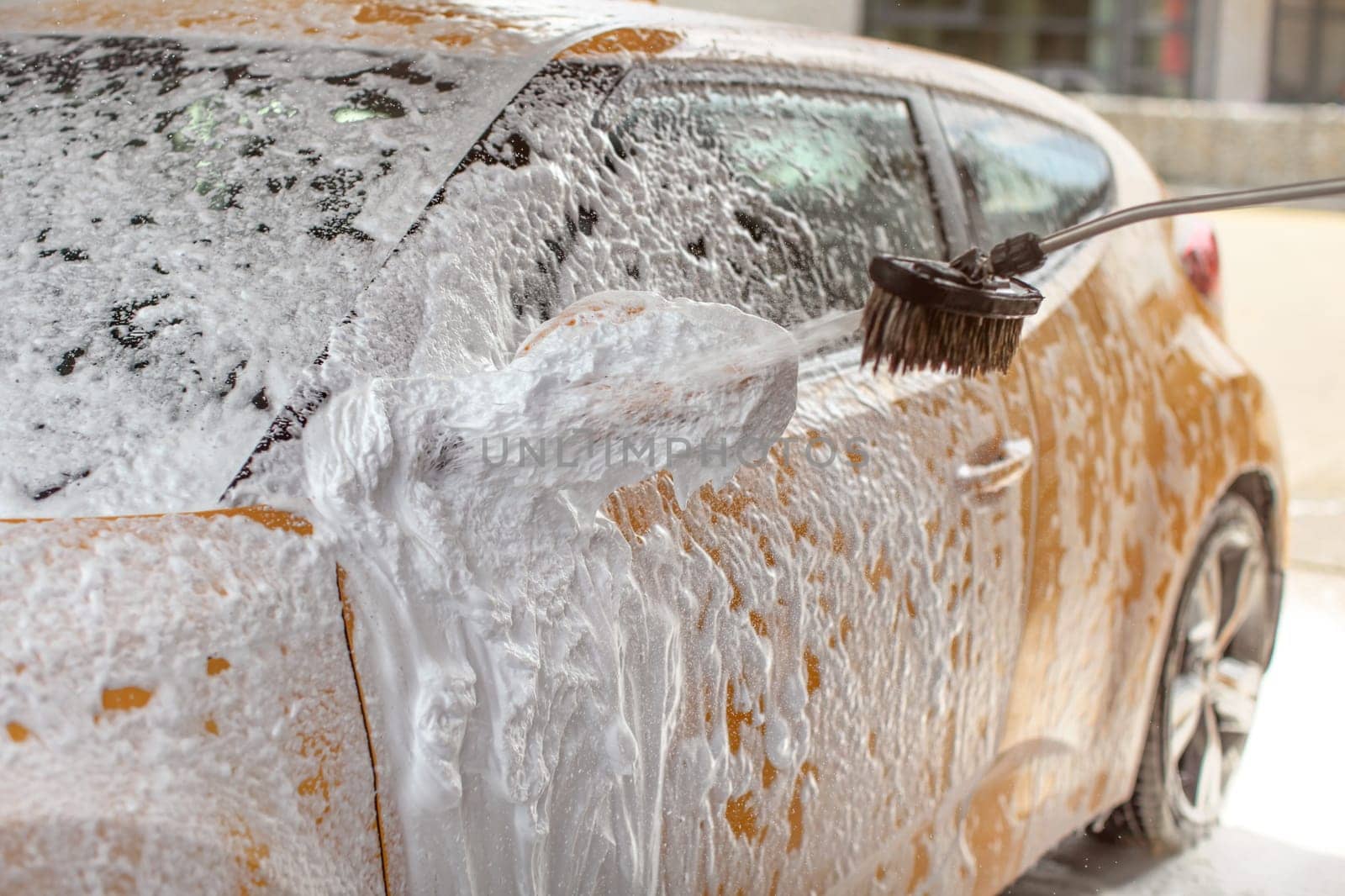 Yellow car washed in self service carwash. Shampoo  spraying to side mirror, already covered in white foam, drops spraying everywhere.