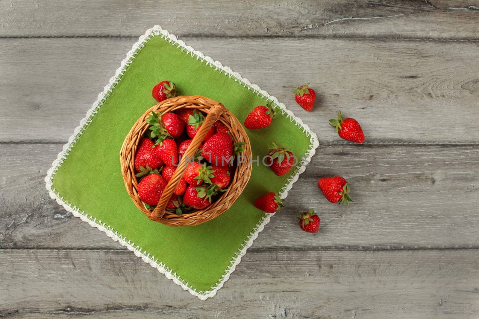 Tabletop view, small basket full of strawberries, some of them spilled on green table cloth under it.