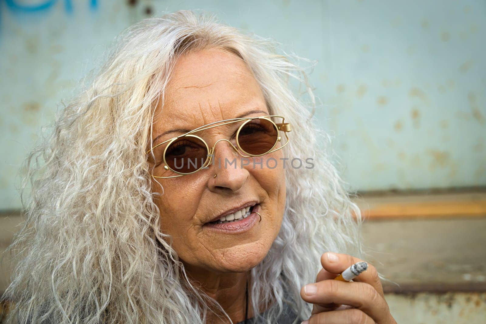 Beautiful woman with long bright curly hair is smoking a cigarette.