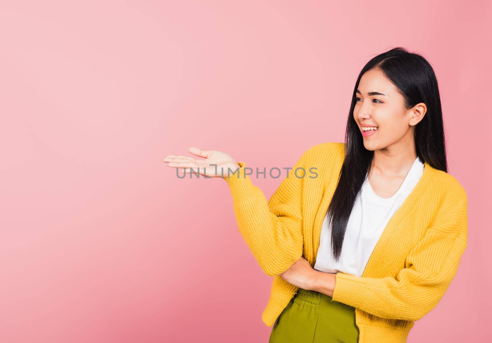 Asian happy portrait beautiful cute young woman smile standing presenting product holding something on palm away side, studio shot isolated on pink background with copy space, female show hand gesture