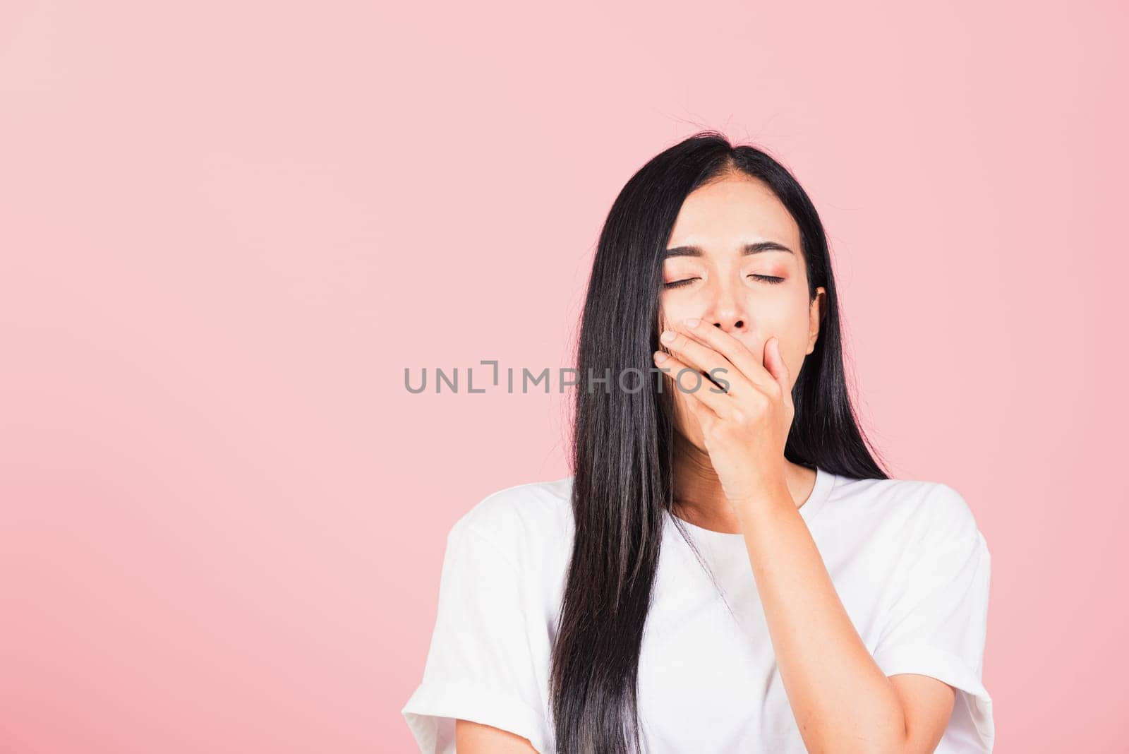 Portrait Asian beautiful young woman emotions tired and sleepy her yawning covering mouth open by hand, studio shot isolated on pink background, Thai female insomnia concept