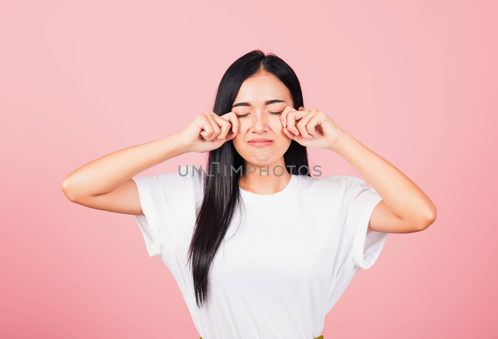 Asian portrait beautiful cute young woman bad mood her cry wipe tears with fingers, studio shot isolated on pink background, Thai female feeling sad unhappy crying with copy space