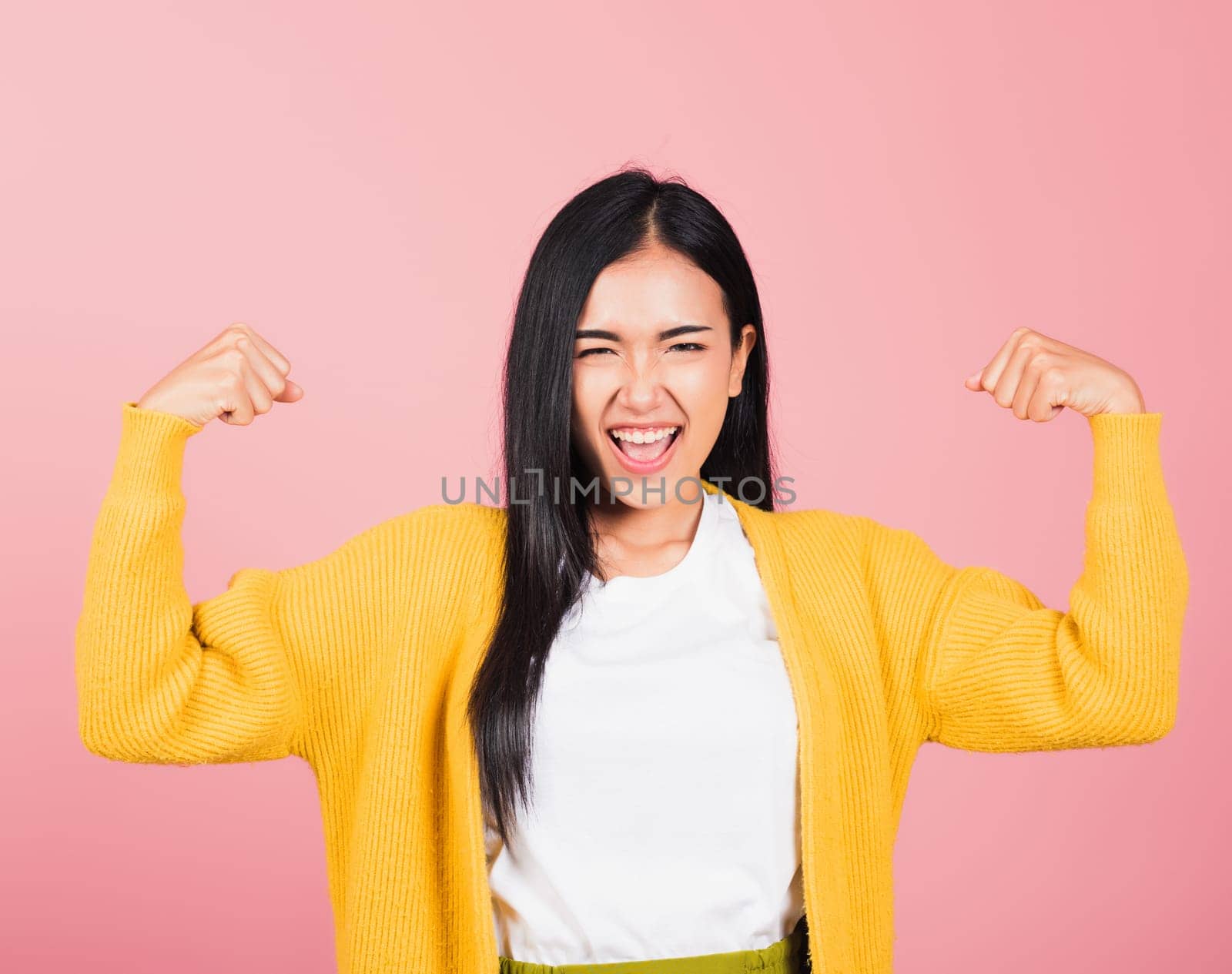Portrait Asian of happy beautiful strong muscles young woman raises arms biceps confident showing power and strength have feeling independent victory successful, studio shot isolated pink background