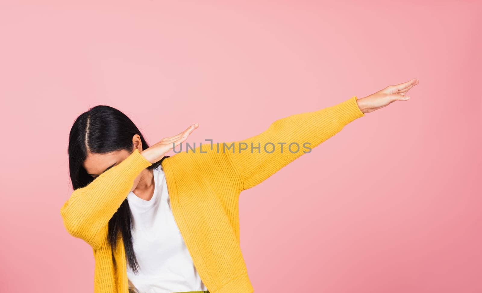 Asian happy portrait beautiful cute young woman teen smile standing move showing DAB dance against gesture raise hands arms covering  face isolated, studio shot on pink background with copy space