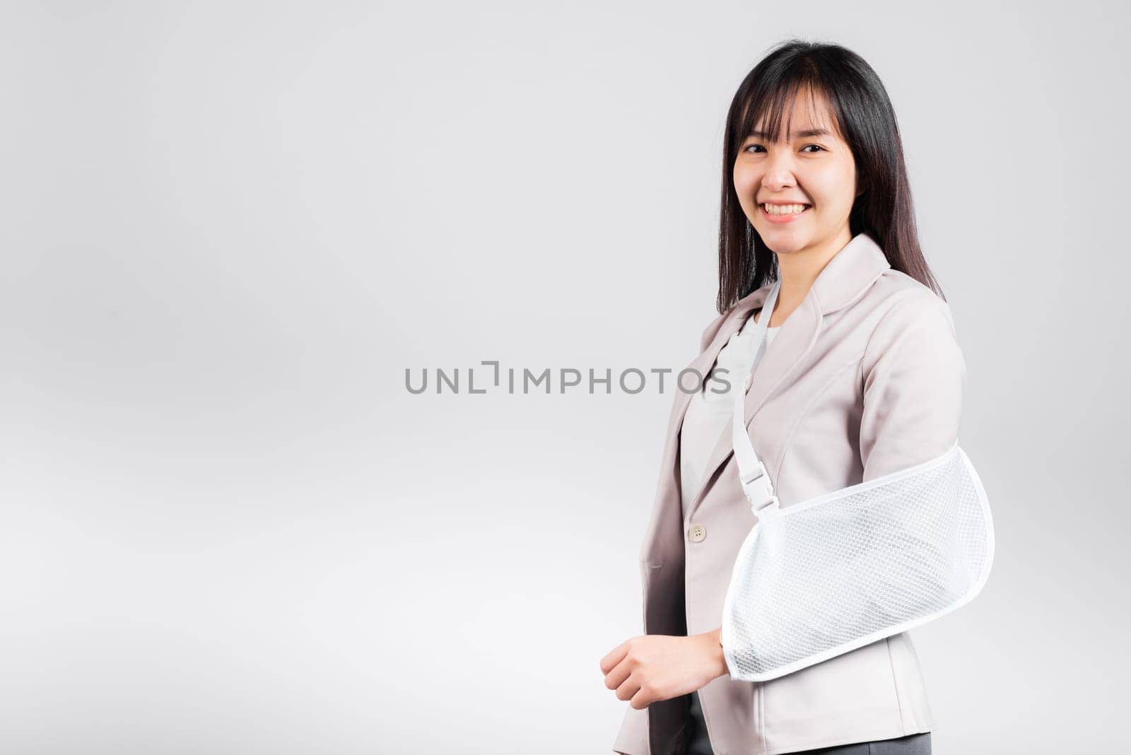 Arm broken. Business woman confident smiling broken arm after accident and wear arm splint for treatment, excited happy Asian female sling support hand studio isolated on white background, copy space