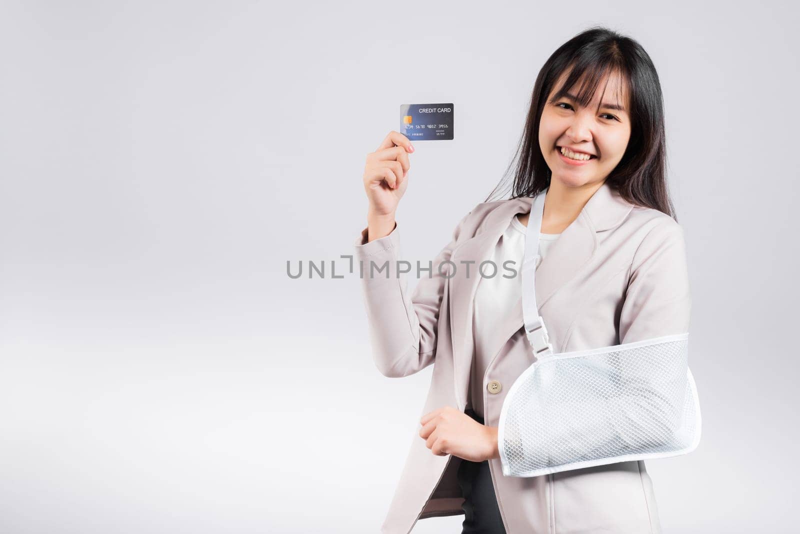 Woman confident smile broken arm after accident and wear arm splint for treatment she emergency pay medical bills by credit card, Happy Asian female sling support hand isolated on white background