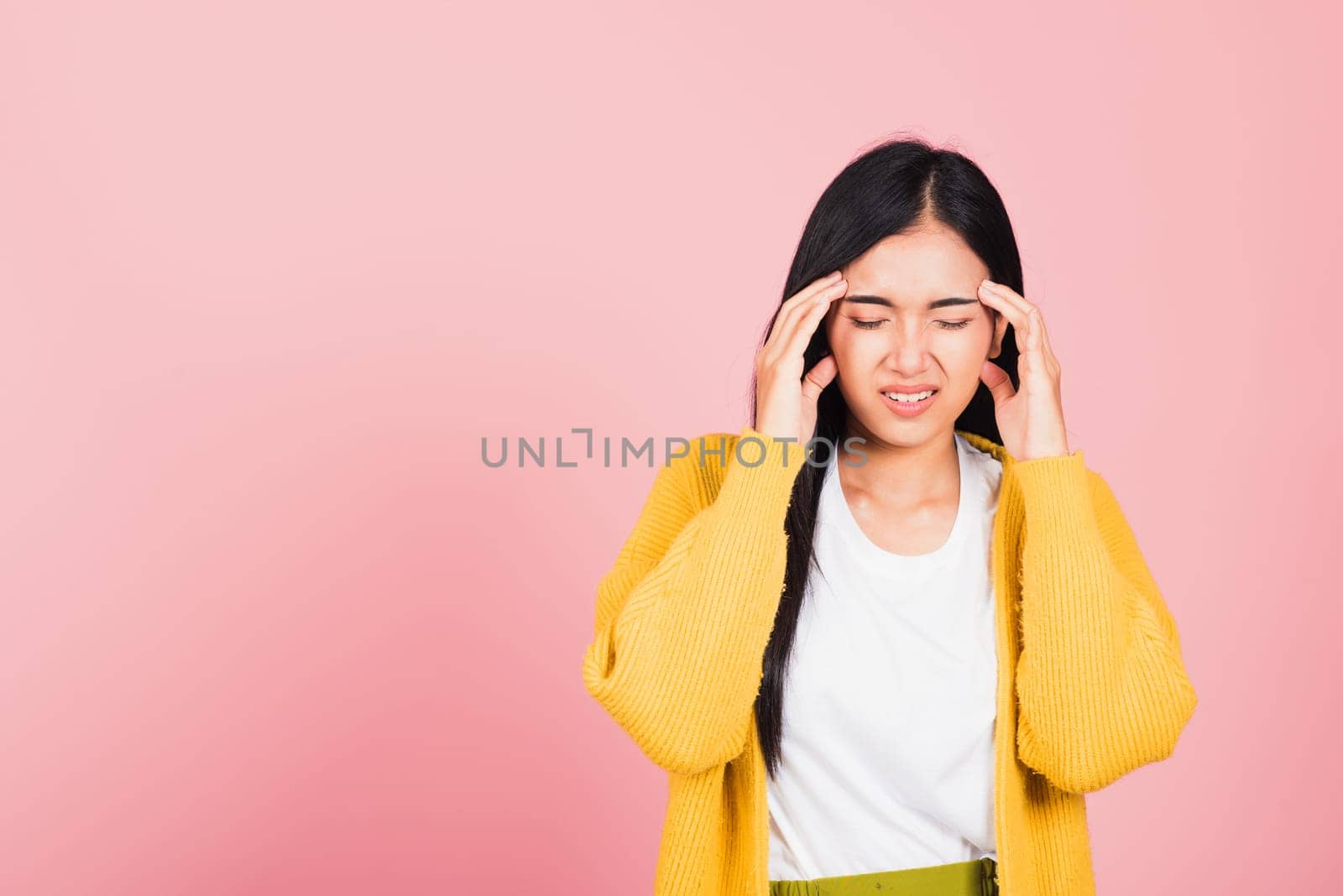 Portrait of beautiful Asian young woman sad tired strain face holding hold head by hands, female person closed eyes problem she headache, studio shot isolated on pink background