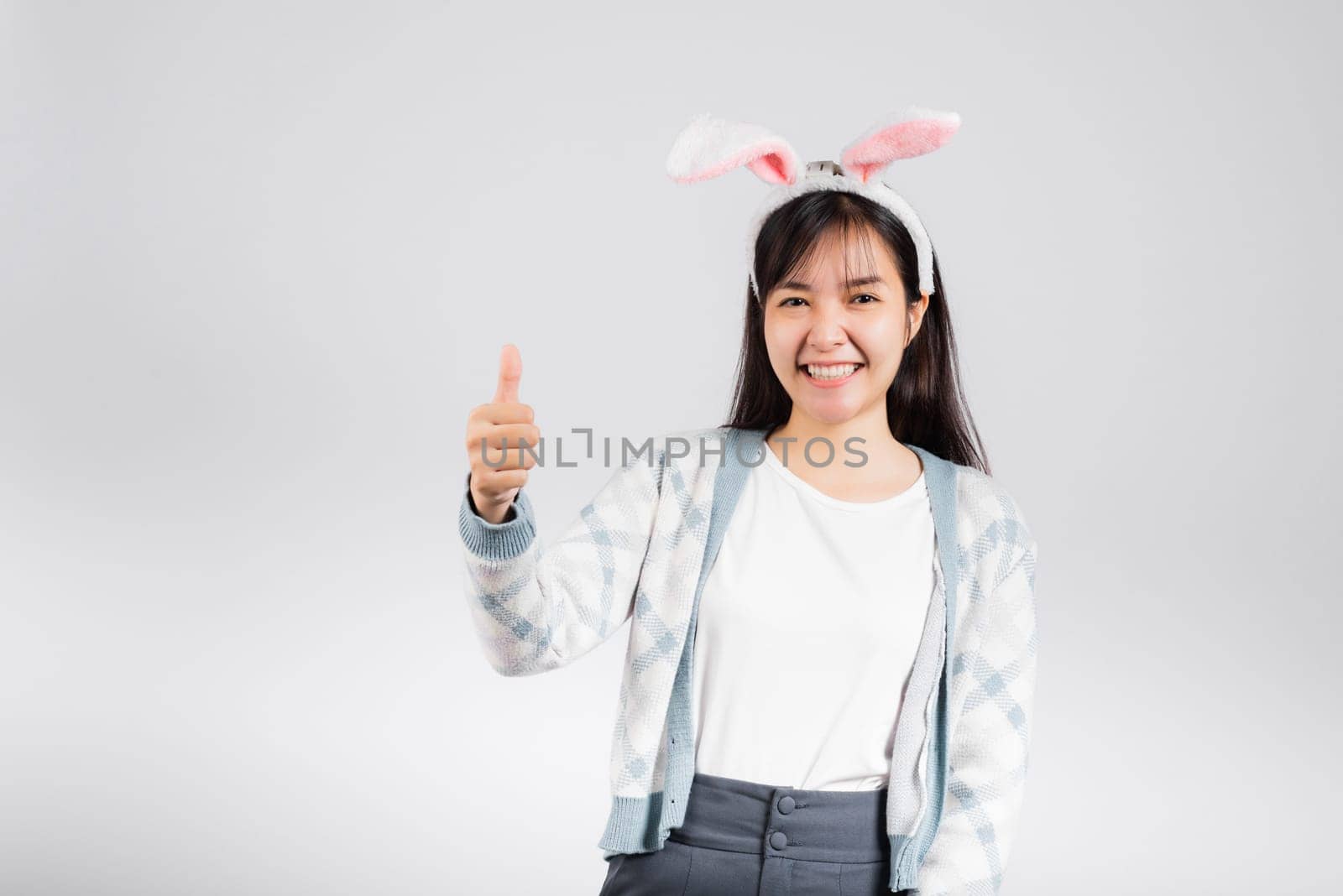 Easter day concept. Smiling happy woman wearing rabbit ears show thumb up for good sign, studio shot isolated on white background with copy space