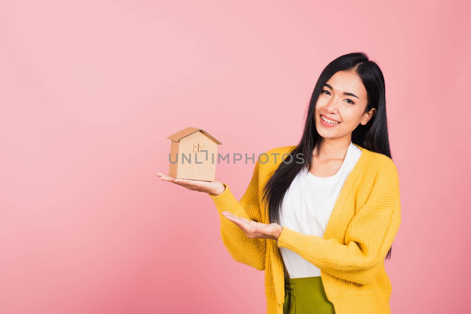 Happy Asian portrait beautiful cute young woman excited smiling holding house model on hand, studio shot isolated on pink background, broker female hold home real estate insurance and banking concept