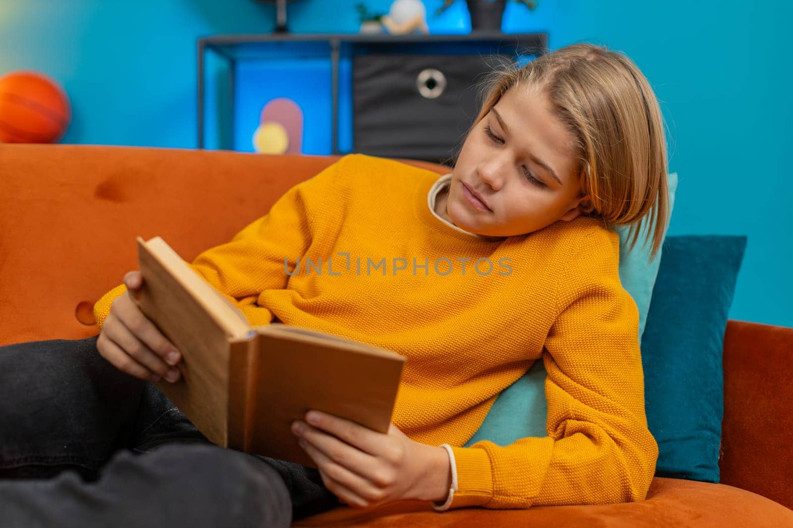 Caucasian teenager boy enjoys reading a book at home. Enthusiastically flips through pages, occasionally looking thoughtfully while lying comfortably on sofa, showing concentration and enjoyment