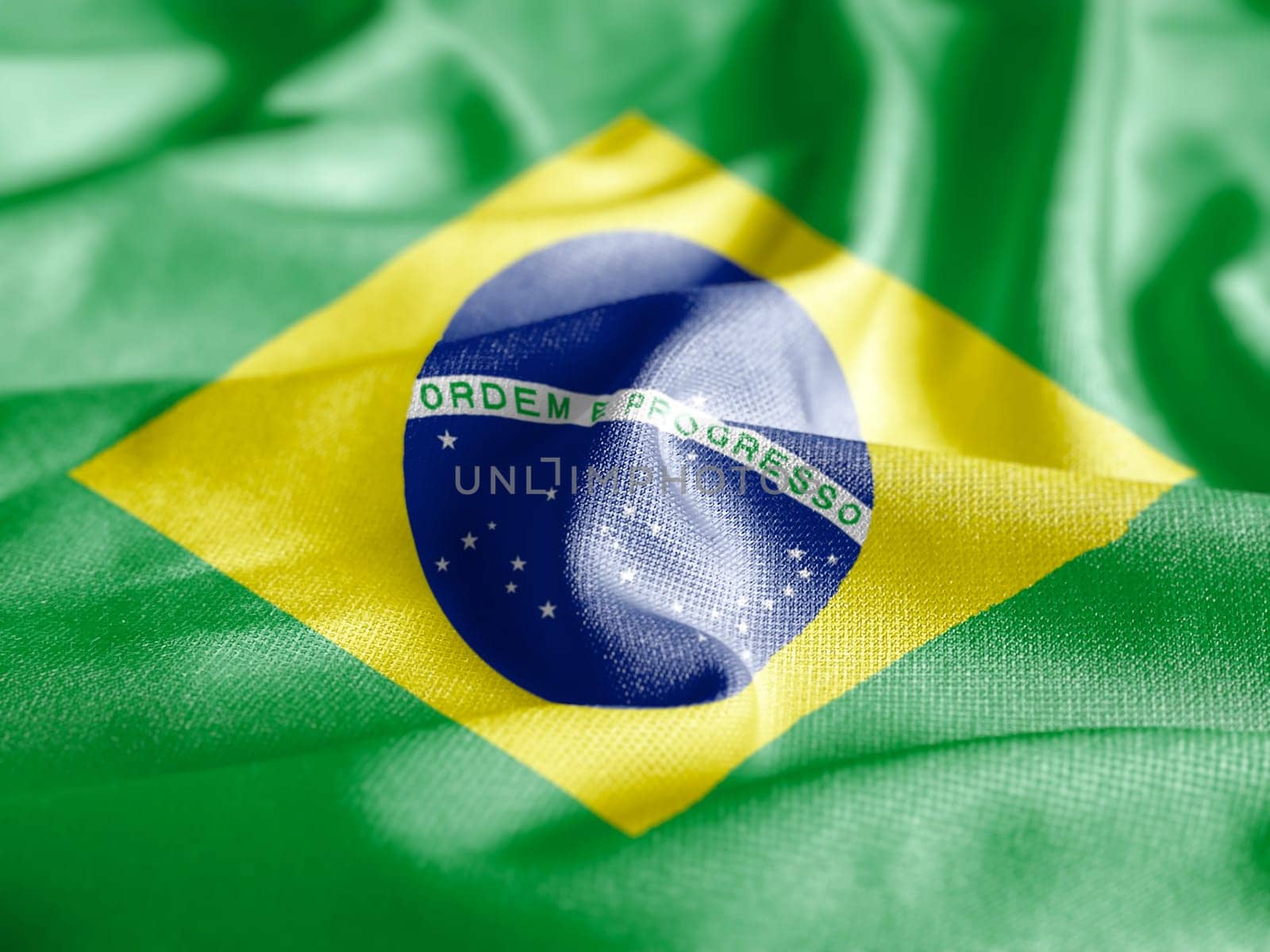Close up of the national flag of Brazil on a ruffled fabric. Curves and folds of the satin fabric with texture. Selective focus and depth of field. Democracy and politics. South american country.
