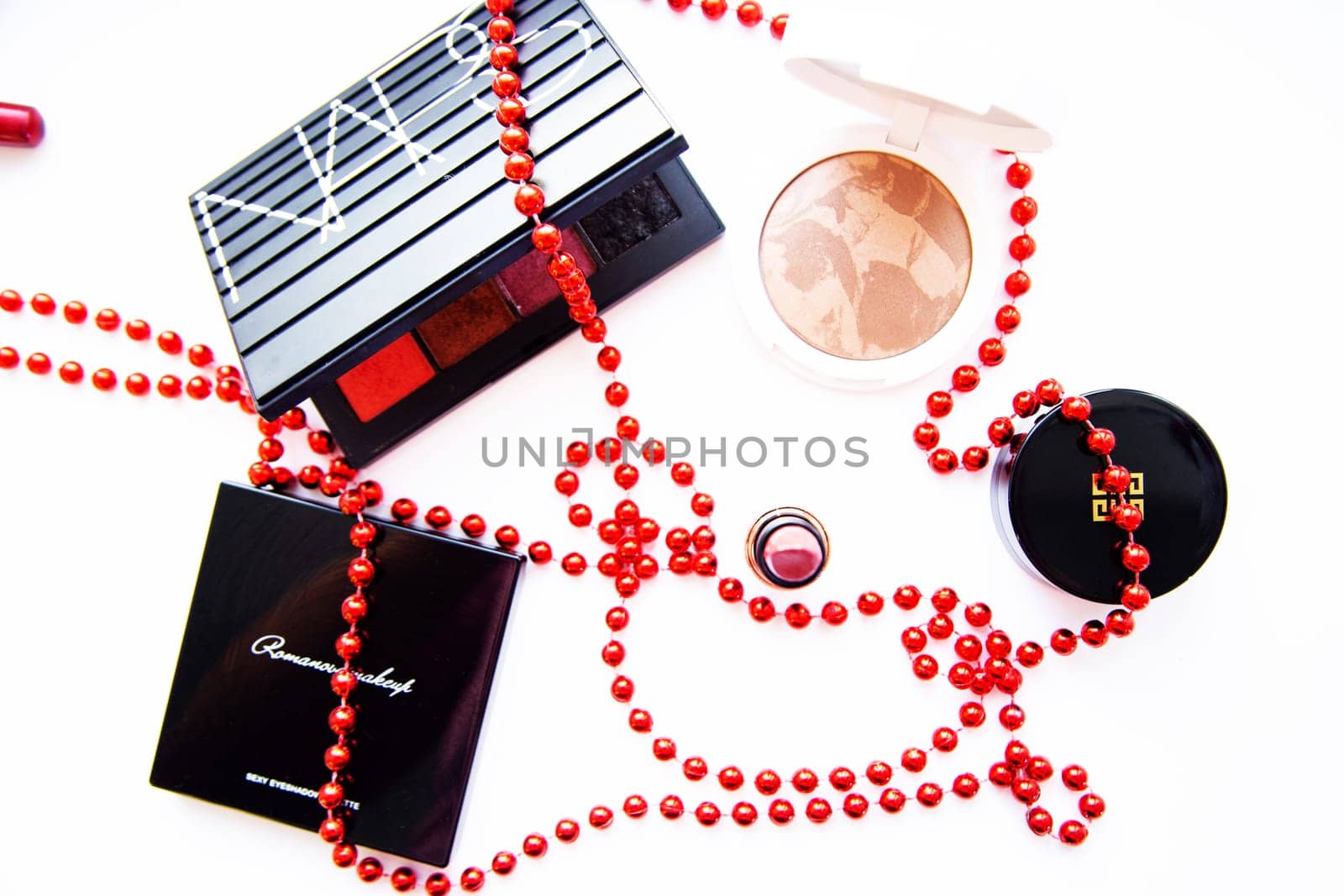 Moscow, 2021. White powder and bronzer, packages with eye shadow, lipstick, blush and a brush of different brands lie on a white background wrapped in red beads. High quality photo