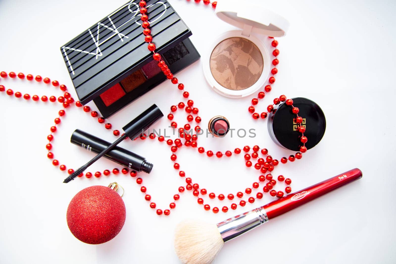 Moscow, 2021. White powder and bronzer, packages with eye shadow, lipstick, blush and a brush of different brands lie on a white background wrapped in red beads and a New Year's red ball. High quality photo