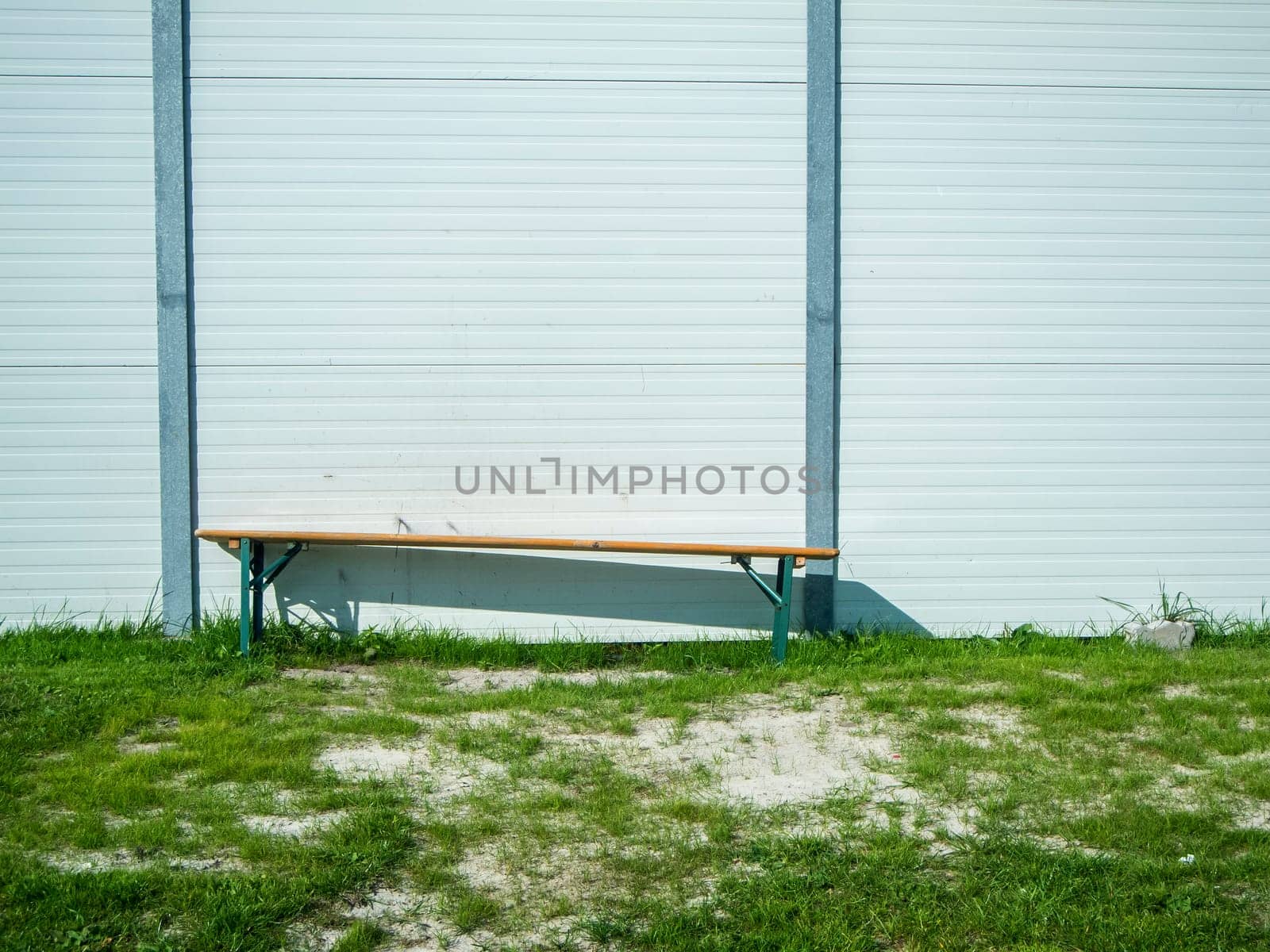 Single foldable beer tent bench on a lawn on a lightweight wall.
