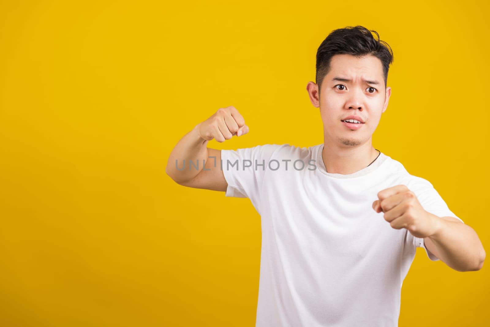 Asian handsome young angry man showing punch a clenches fist, aggressive male punching towards the camera looking to camera, studio shot isolated on yellow background