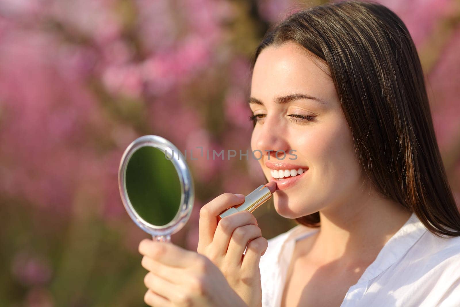 Happy woman painting lips in nature
