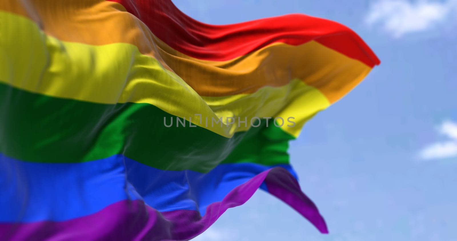 the rainbow flag waving in the wind in a clear day. Symbol of lesbian, gay, bisexual, transgender (LGBT) and queer pride and LGBT social movements. Selective focus
