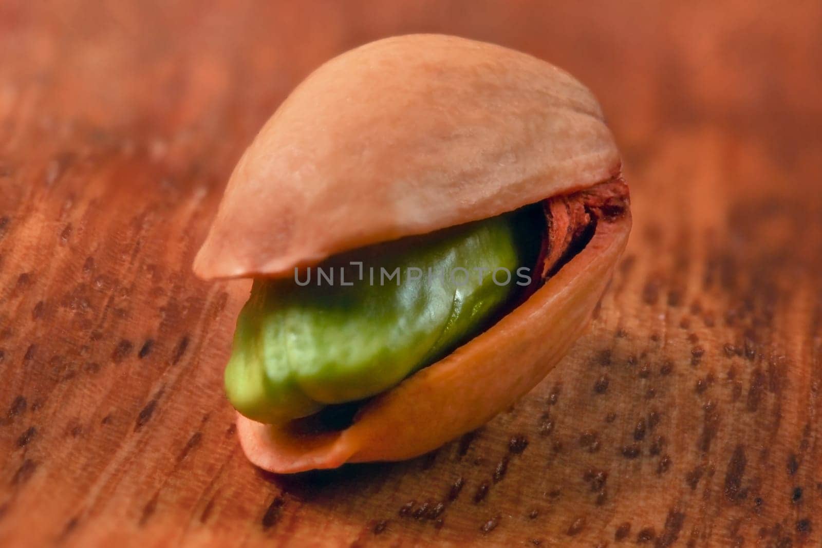 Shallow depth of field (extreme close up) single pistachio in shell, green nut visible, on wooden board.