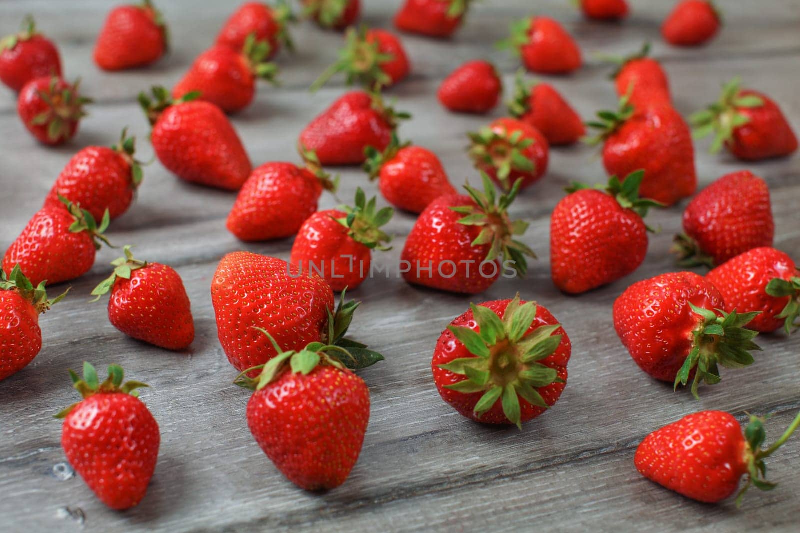 Red ripe strawberries spilled on gray wood desk.