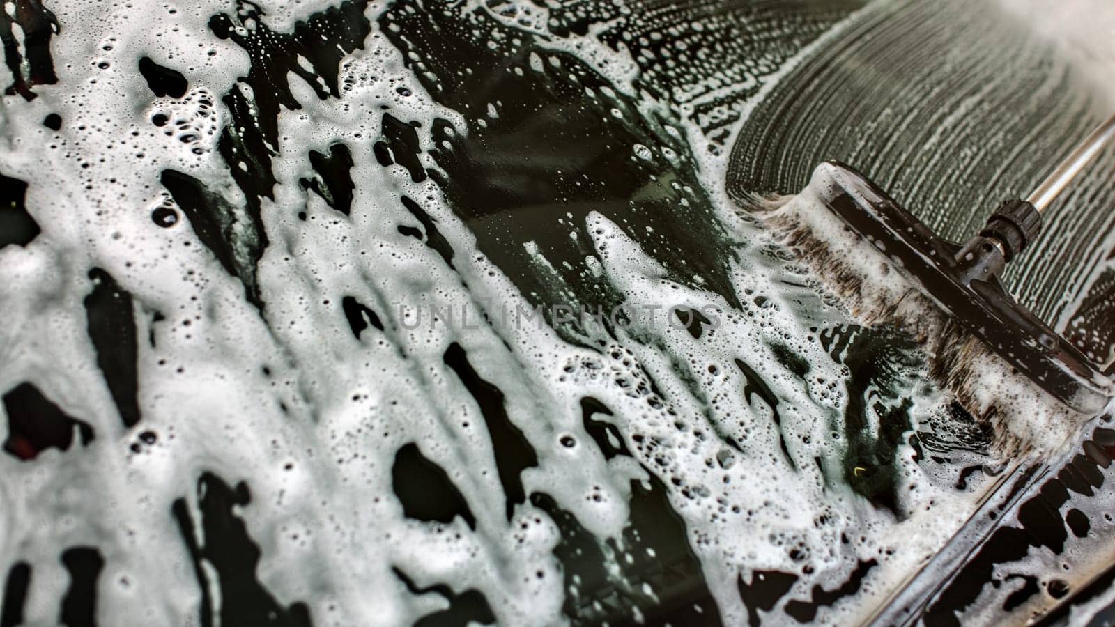 Widshield of a car being washed in self serve carwash, brush leaving strokes in white shampoo and foam on glass.