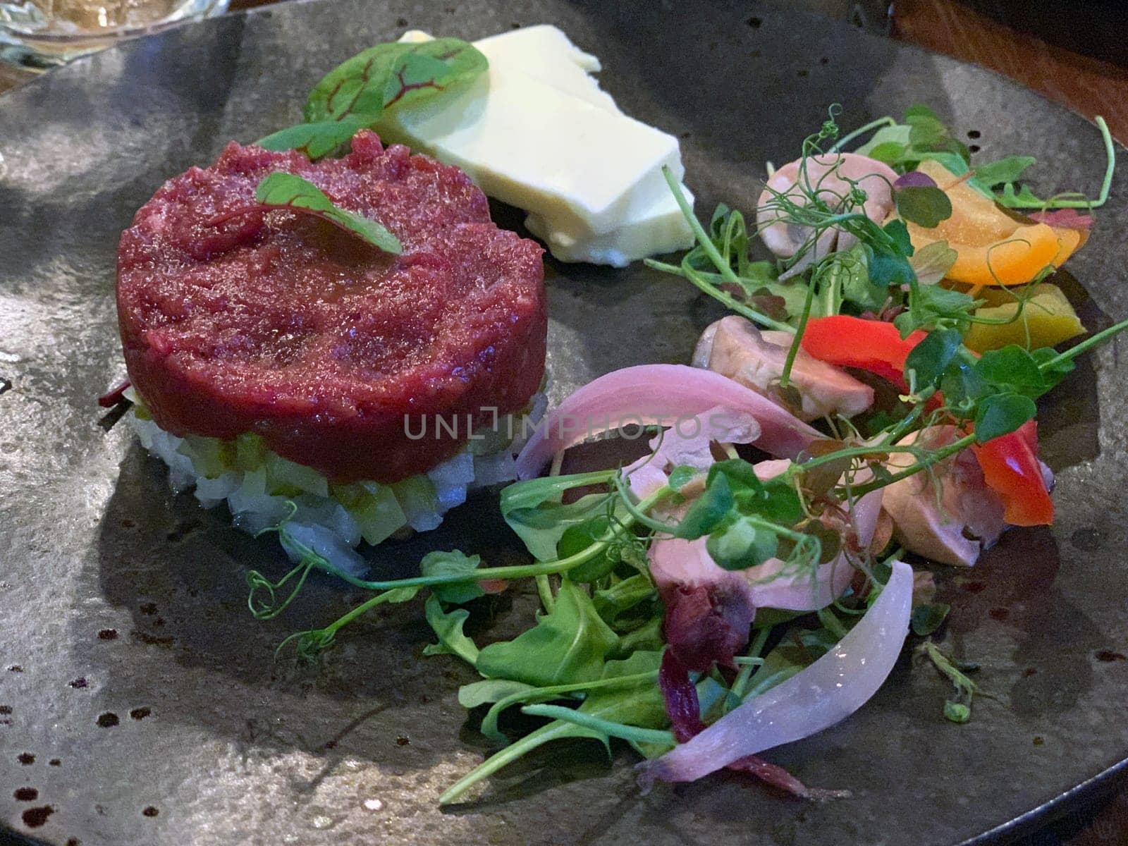 The raw meat tartare with greens and rice on a black dish composition