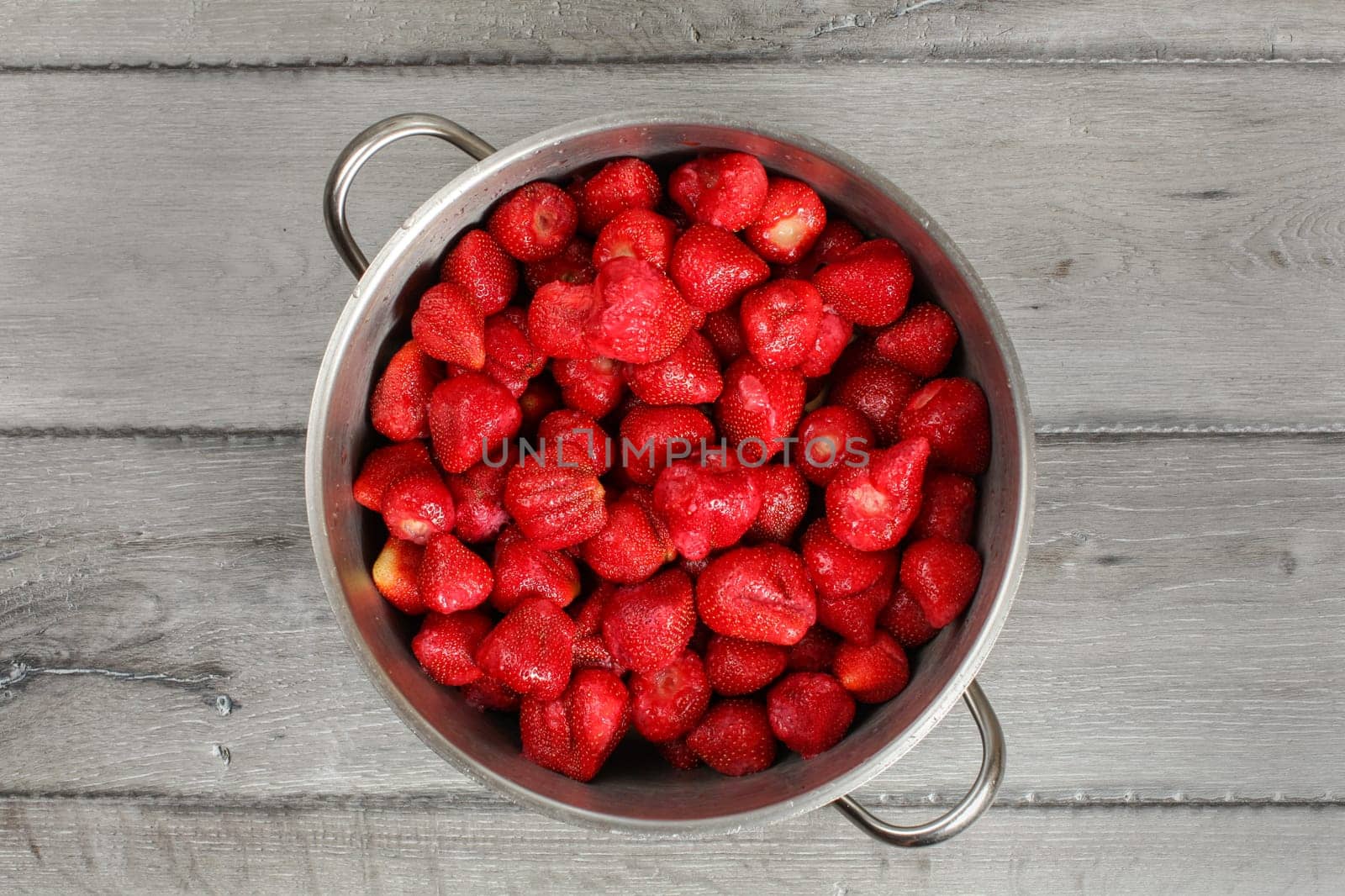 Tabletop view, steel pot full of strawberries with leaves removed. Homemade strawberry jam preparation.