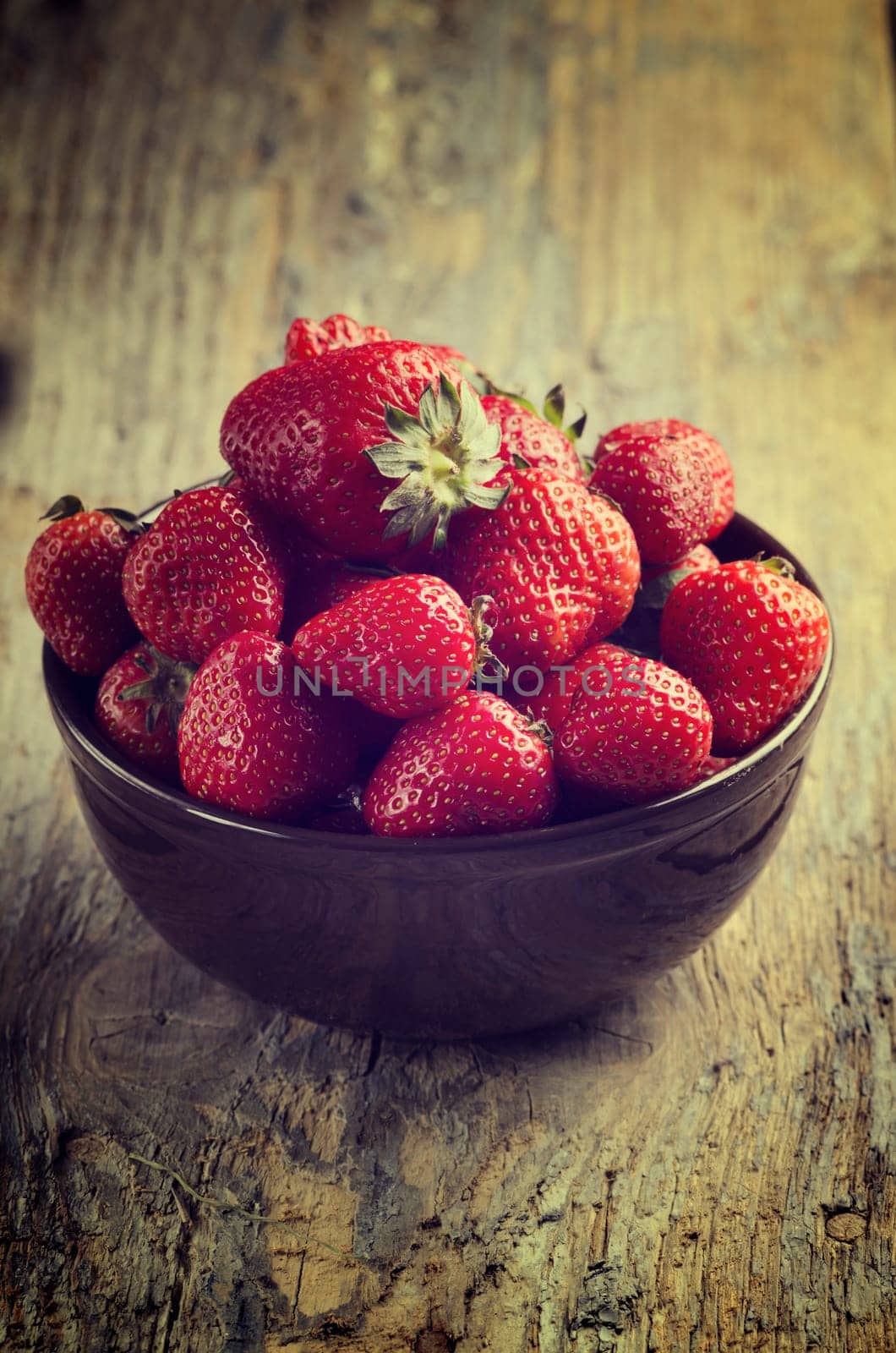 Strawberries in bowl on rustic table. Cross processed