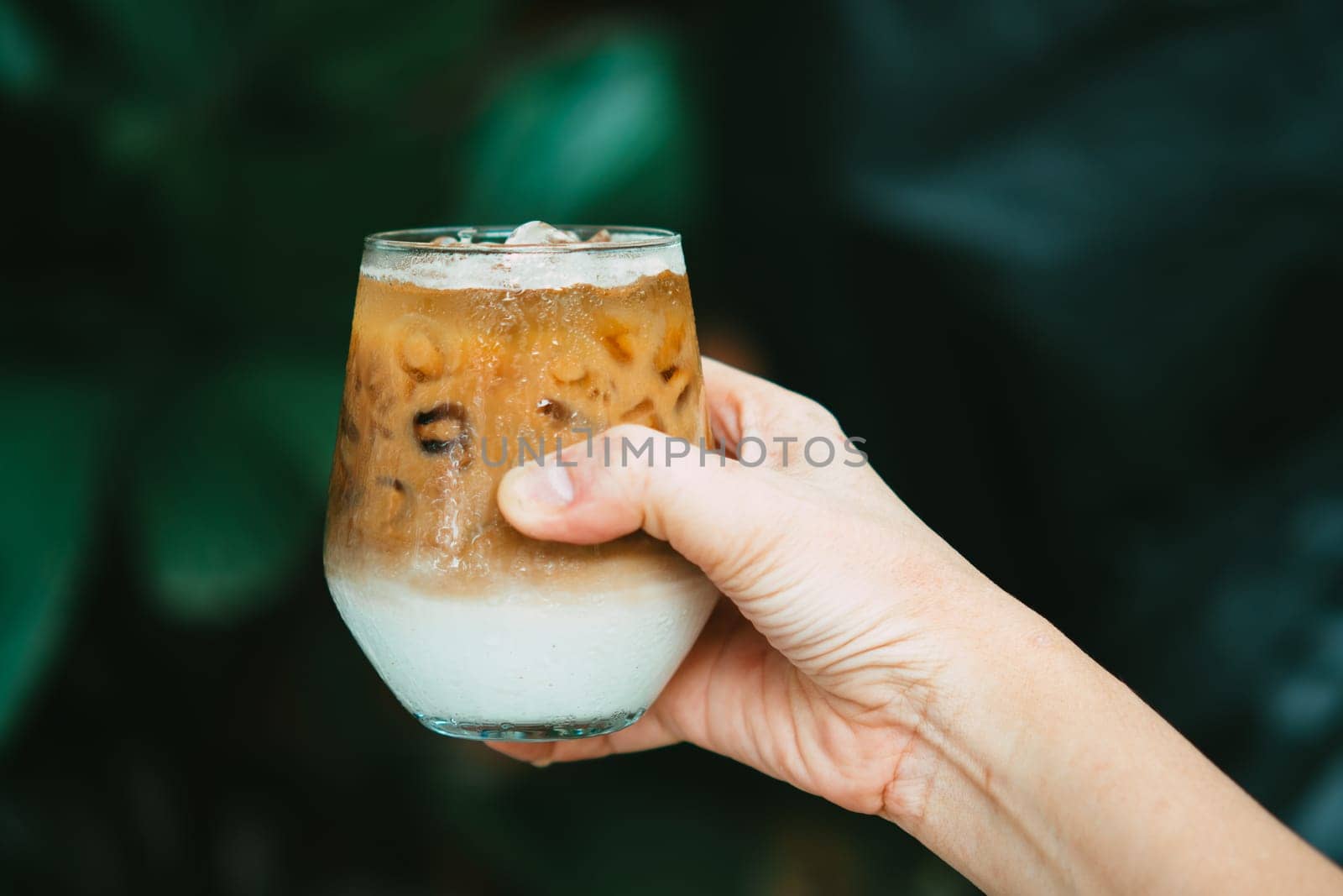 Hand hold iced latte coffee in a glass with cream on bottom . cold summer drink background