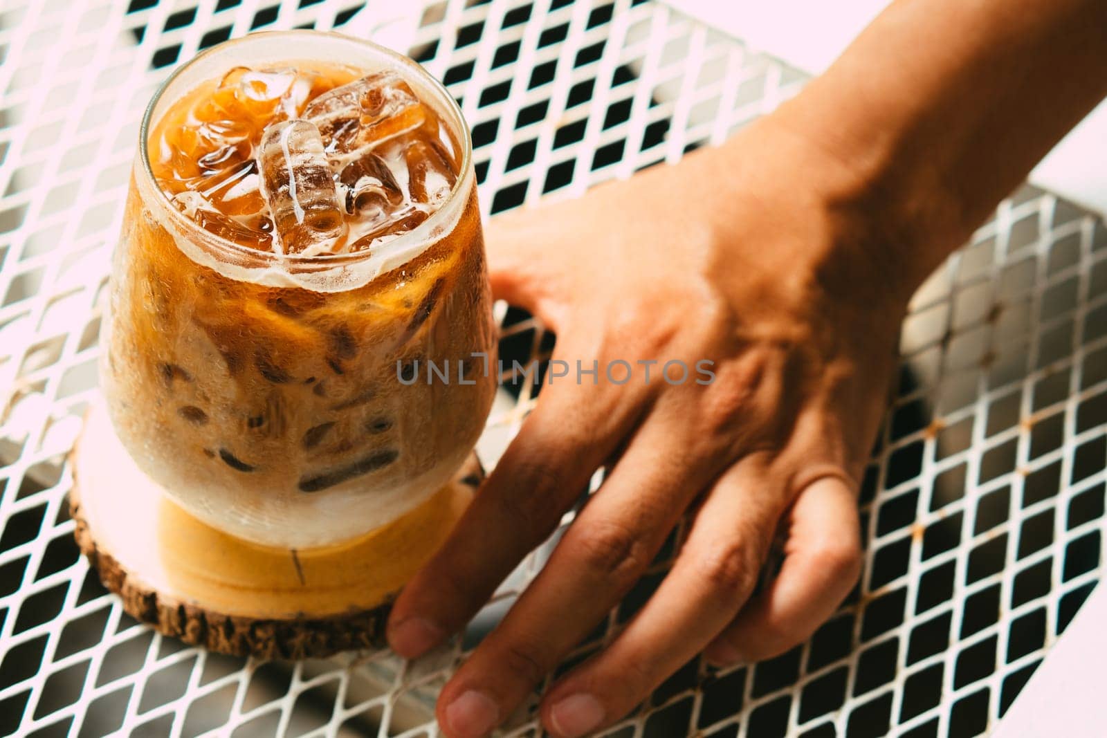 Hand hold iced latte coffee in a glass with cream on bottom . cold summer drink background