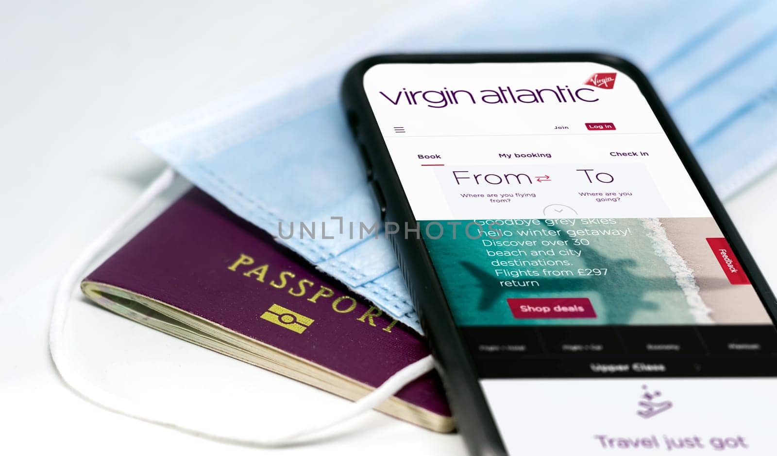 London, UK, July 2021: phone with the Virgin Atlantic airlines app on the screen lying over a protective mask and a passport. Travel safety and restrictions during coronavirus pandemic