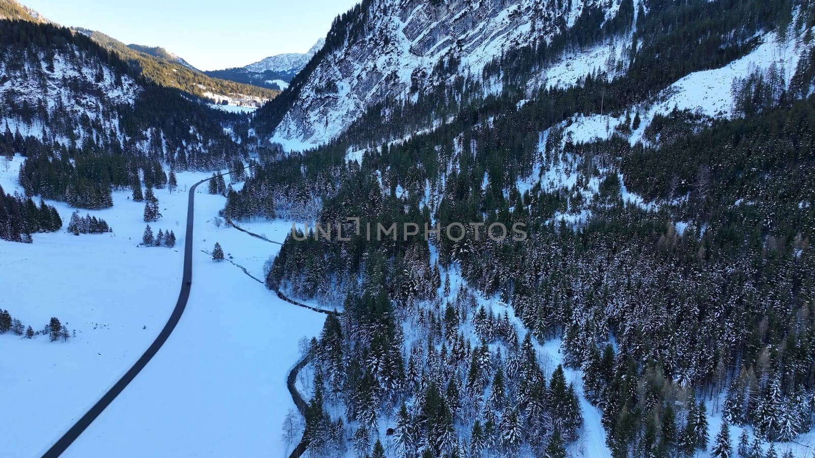 Aerial drone shot of snowy landscape with road and mountain forest