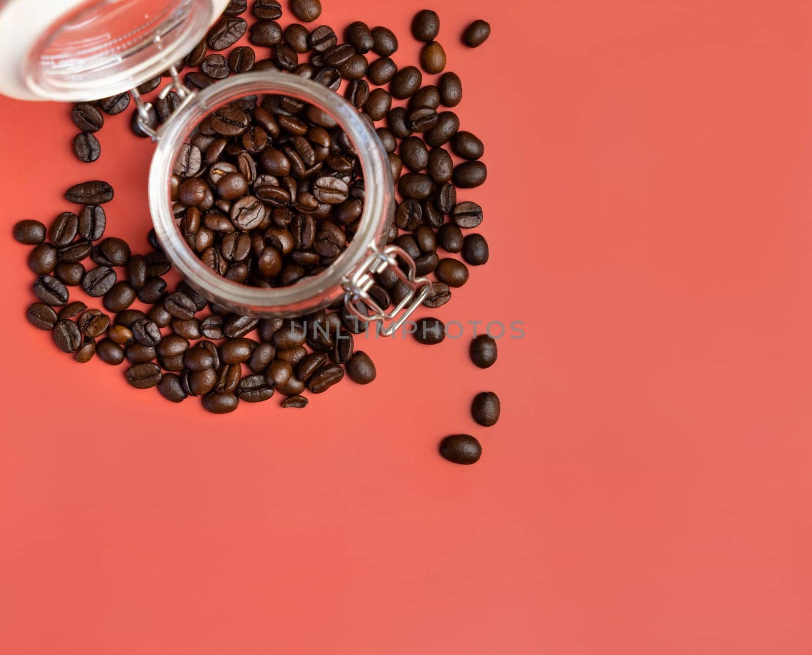 Roasted Coffee beans in a glass jar top view on pink background with copy space. Represent breakfast, energy, freshness or aroma