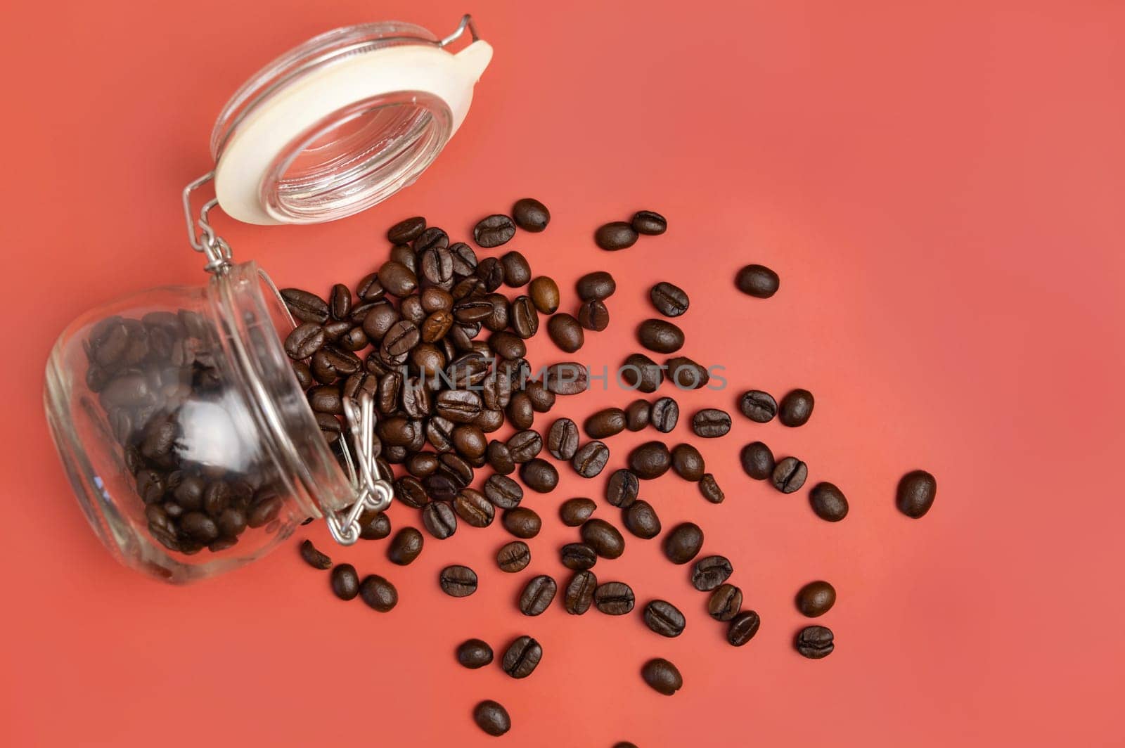 Roasted Coffee beans in a glass jar top view on pink background with copy space. Represent breakfast, energy, freshness or aroma