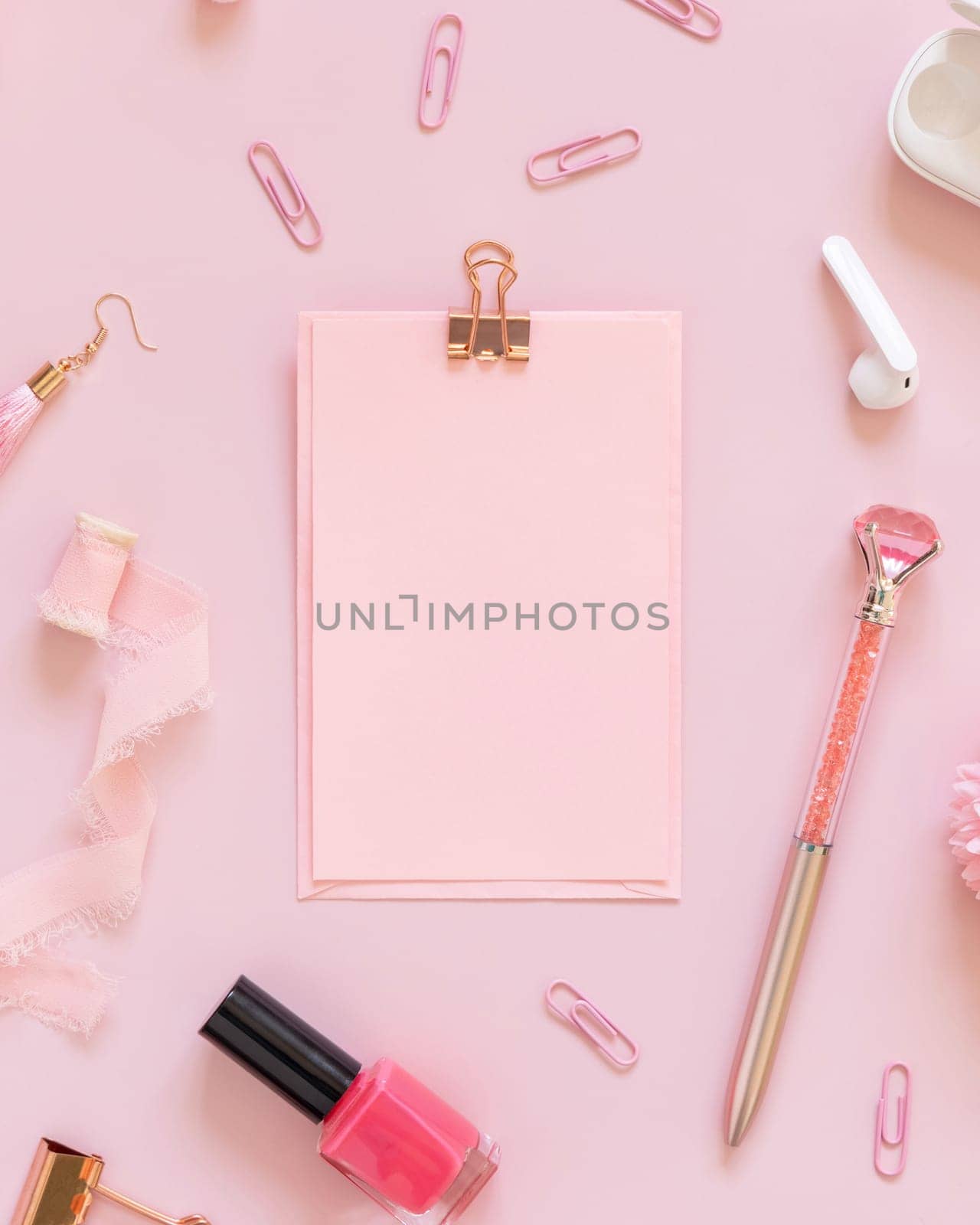 Paper with a clip and Pink school accessories on pastel pink, top view, textbook mockup. Girly workplace with scissors, pencils, pen, paperclips, earrings and watch. Back to school concept