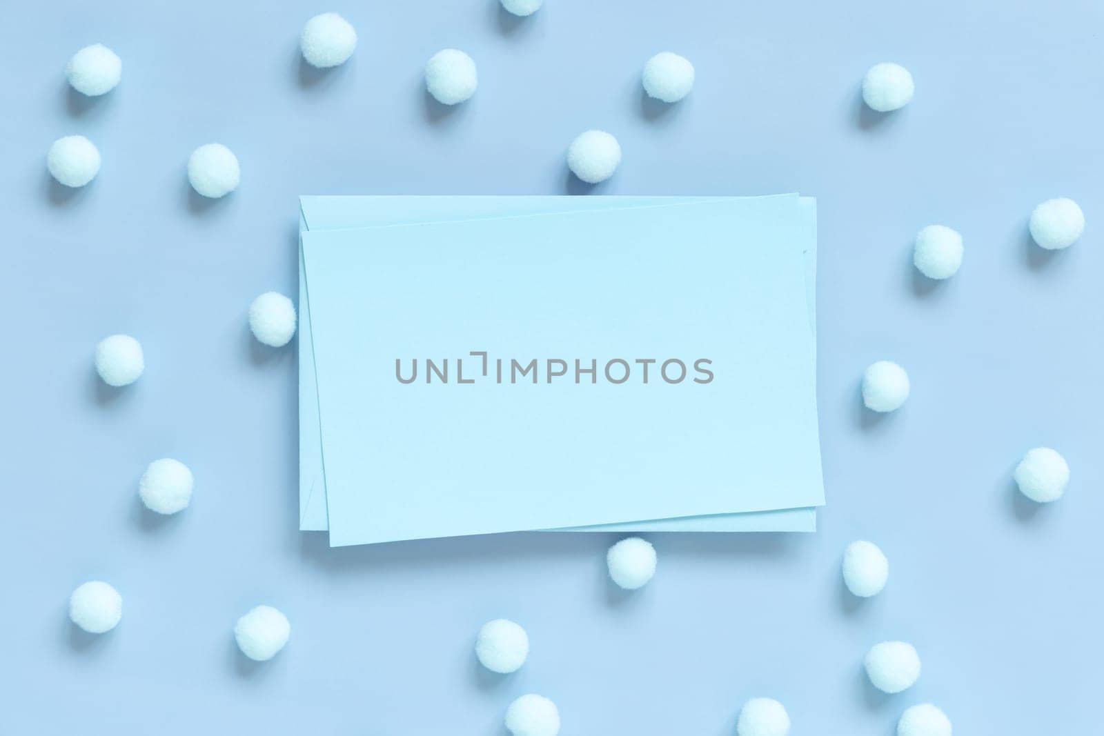 Blank card between pastel pom-poms on light blue top view. Romantic scene with blank horizontal card with place for text flat lay. Spring or boyish concept