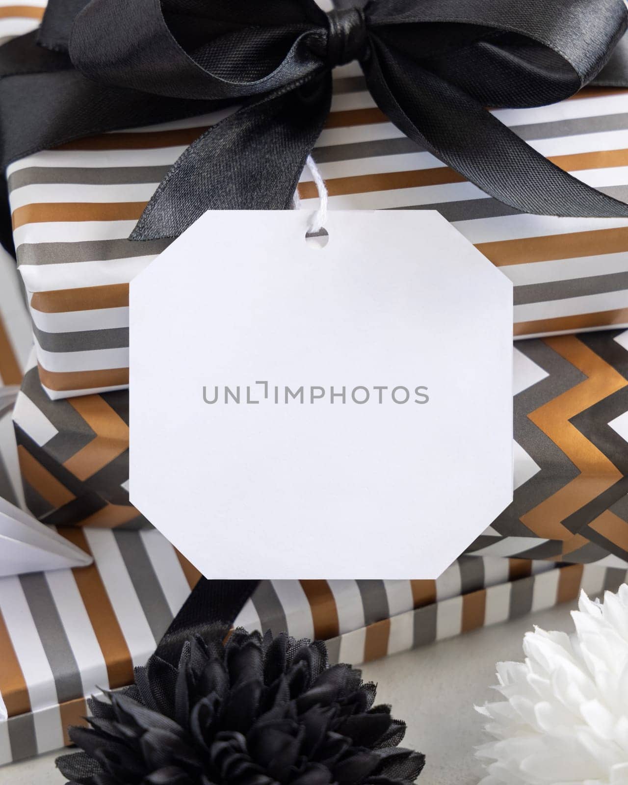 Present with blank gift tag and black bow close up. Gift boxes wrapped in Striped and chevron geometric paper near black and white decor. Christmas, New Year, Birthday, Anniversary label mockup