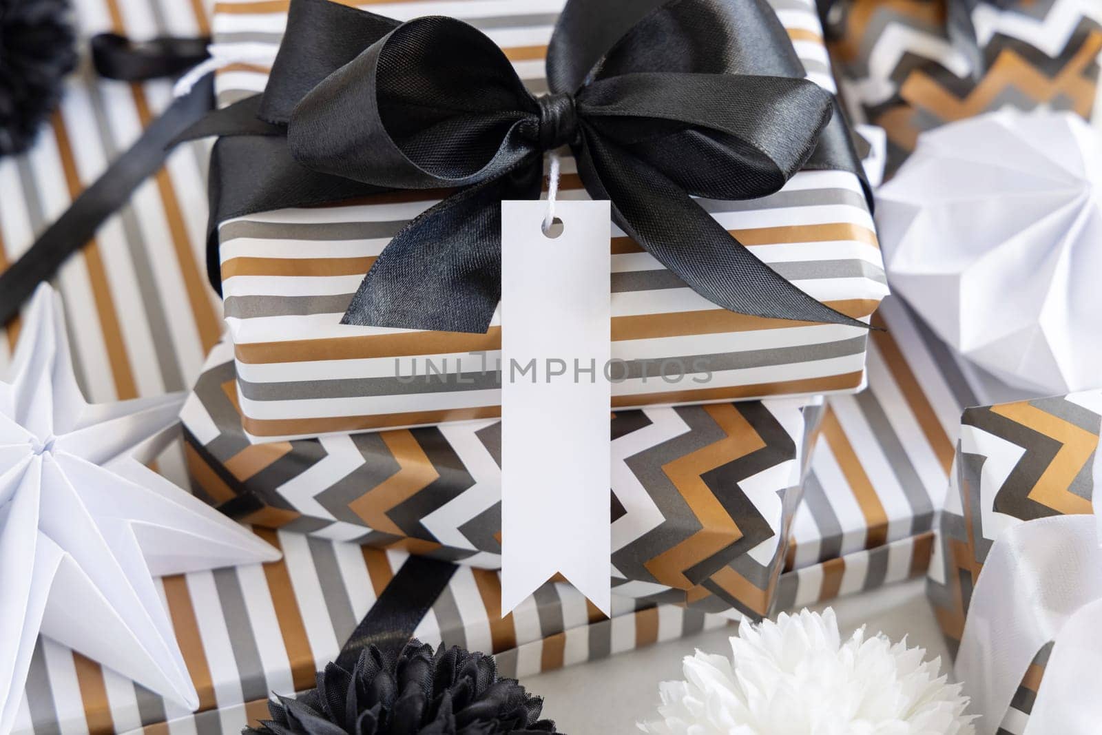 Present with blank vertical gift tag and black bow close up. Gift boxes wrapped in Striped and chevron geometric paper near black and white decor. Christmas, New Year, Birthday, Anniversary label mockup