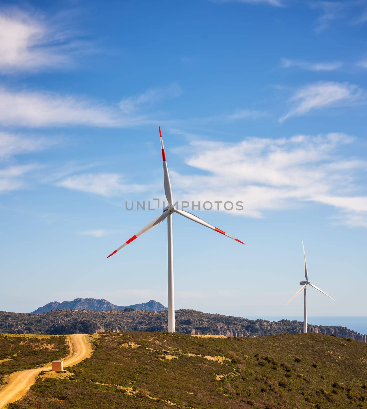 Wind turbines on a beautiful blue sky with clouds in a mountain wind farm in Sardinia. Renewable energy concept, green energy generation. Energy industry.