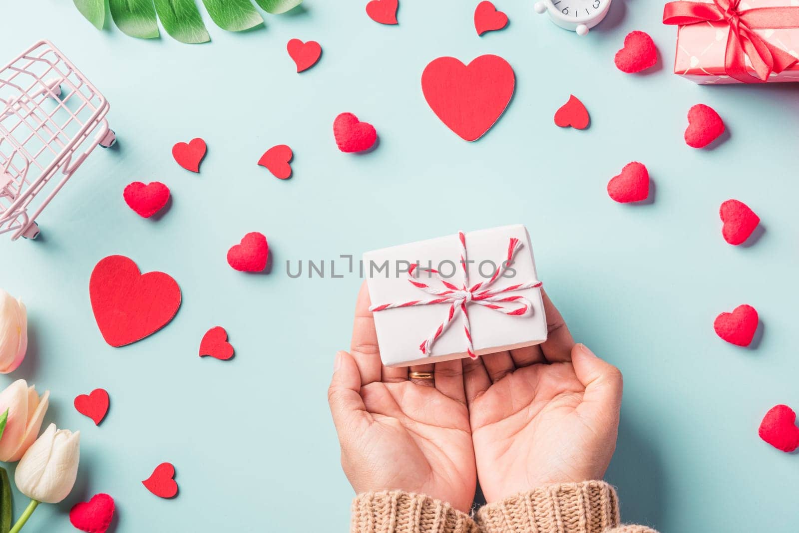 Valentine's day and birthday. Woman hands holding gift or present box decorated and red heart surprise on blue background, Female's hand hold gift box package in craft paper Top view flat lay