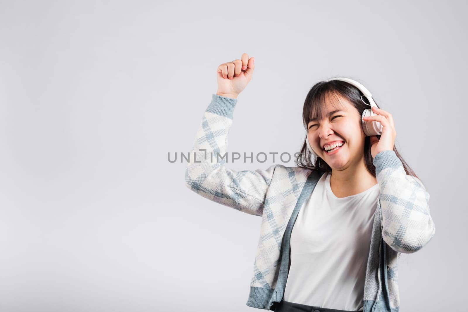 Woman excited smiling listening to music radio in bluetooth headphones and dancing with smartphone studio shot isolated white background, happy Asian young female Karaoke online app in mobile phone
