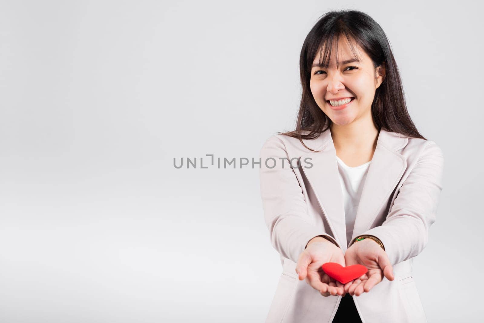 Smiling woman confidence showing holding red heart with her hand palm isolated white background, Asian happy portrait beautiful young female send love and happy valentine in studio shot, copy space